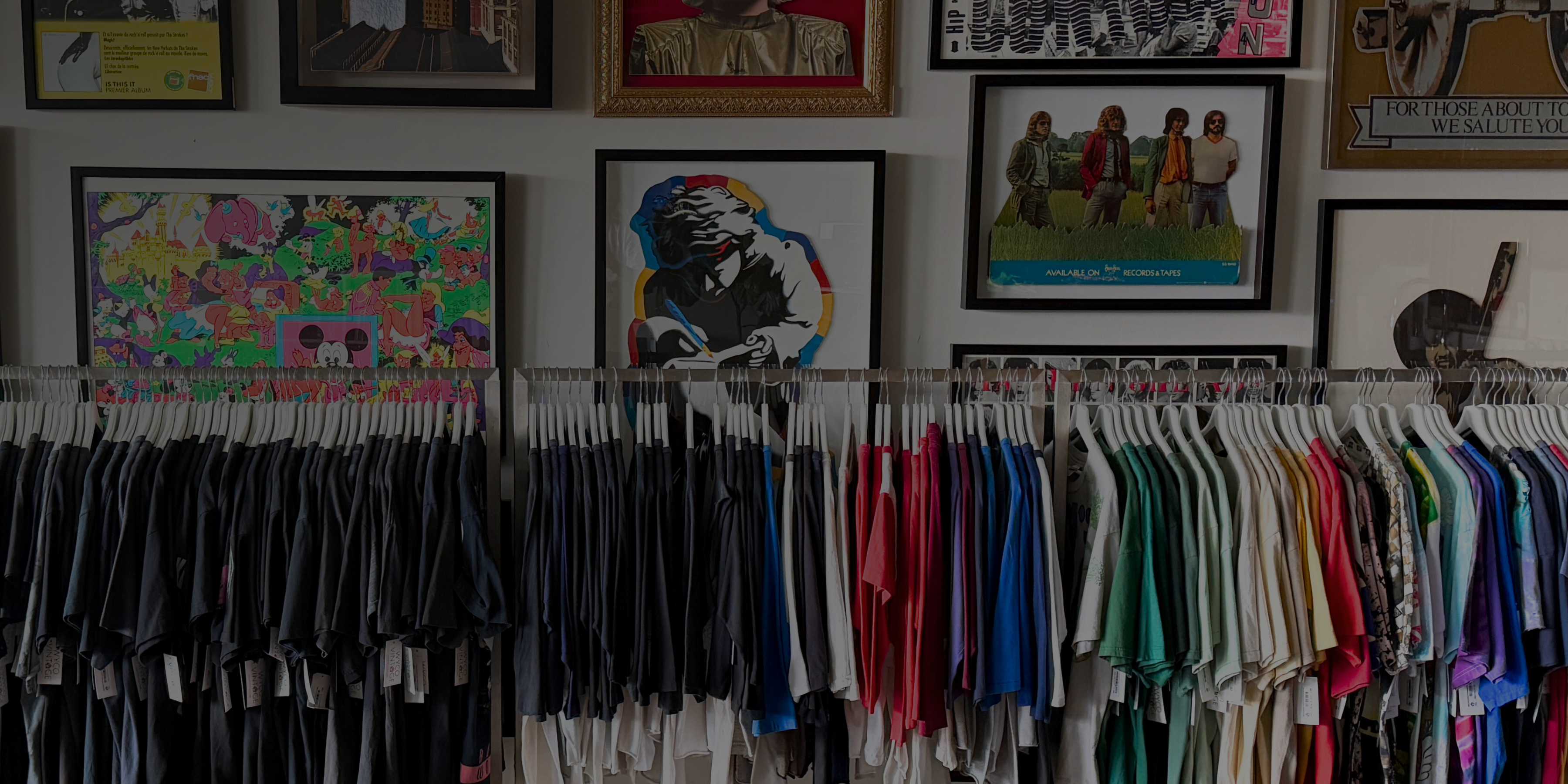 Clothing rack with shirts and a wall of framed artwork in a store.